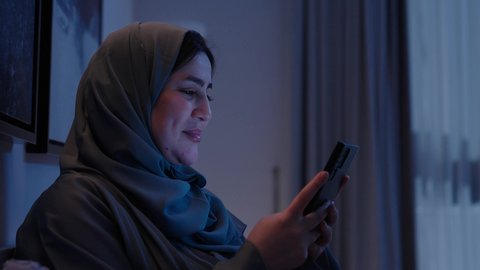 الدردشه مع الأهل والأصدقاء، إيماءات السرور والسعادة، استخدام التكنولوجيا والتقنيات الحديثة المتطورة، تصوير مقرب لامرأة عربية سعودية خليجية محجبة تنظرالي الهاتف، الرد على الرسائل النصيه، استخدام التقنيات والاجهزه الحديثه