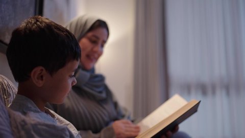 اهتمام الأم بالابناء، امرأة عربية خليجية سعودية ترتدي العباءة و الحجاب تقرأ لإبنها قصه مسلية، ام تقضي وقت ممتع مع الابن قبل النوم، قراءة القصص والروايات، مفهوم السعادة الاسرية،لأنشطة التعليمية وتنميه قدرات الابناء بالتعلم