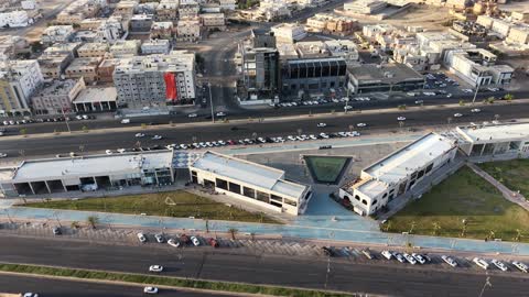 A place for shopping and having a good time, an entertainment and commercial center, modern and advanced architectural engineering art in the Kingdom of Saudi Arabia, distinctive restaurants, cafes, and shopping centers, drone footage of the My Walk complex on Amr Ibn Al-As Street in the Al-Musayf neighborhood of Tabuk city during the daytime.