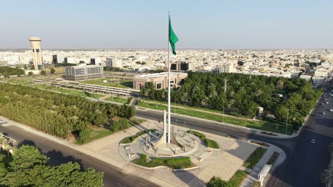 الفخر والاعتزاز بالانتماء الى الوطن,تصوير درون لسارية العلم السعودي الأخضر المرفرف في الهواء في مدينة تبوك،  المعالم المشهورة في المملكة العربية السعودية ،حركة مرور السيارات في شوارع المدينة