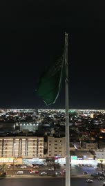الفخر والاعتزاز بالانتماء الى الوطن,تصوير درون لسارية العلم السعودي الأخضر المرفرف في الهواء في مدينة تبوك،  المعالم المشهورة في المملكة العربية السعودية ،حركة مرور السيارات في شوارع المدينة