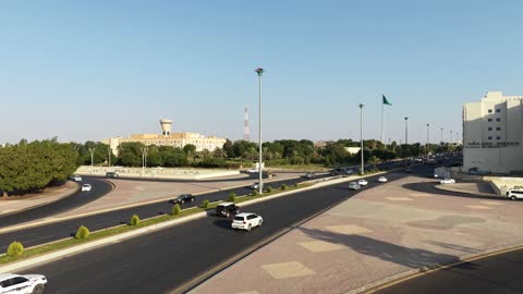 Urban and street engineering, the green Saudi flag flying in the air in the city of Tabuk, famous landmarks in the Kingdom of Saudi Arabia, drone footage of car traffic in the city's streets.