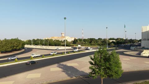 Urban and street engineering, the green Saudi flag flying in the air in the city of Tabuk, famous landmarks in the Kingdom of Saudi Arabia, drone footage of car traffic in the city's streets.