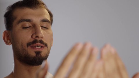 الدعاء والتقرب الى الله، بورتريه لرجل مسلم عربي سعودي خليجي يرتدي ملابس الاحرام يدعي بتضرع وخشوع ويرفع يديه للأعلى، داء فريضة الحج، موسم العمرة في شهر رمضان المبارك، مفهوم الاجتهاد في العبادة, خلفية رمادية