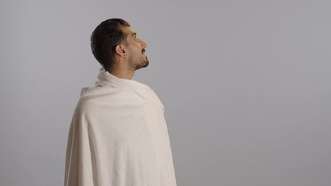 بورتريه مقرب لرجل عربي سعودي خليجي يرتدي زي الاحرام يقوم بشرب المياه العذب،  الارتواء بماء زمزم، الحفاظ على الجسم من الجفاف، أداء مناسك الحج والعمرة، خلفية رمادية