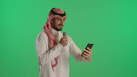 ايماءات الاستمتاع والاندماج، بورتريه لشاب عربي خليجي سعودي يرتدي الثوب التقليدي والشماغ  يحمل بيده مكبر الصوت يقوم بإلقاء الخطاب، خلفية خضراء، كروما