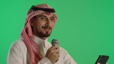 إقامة ورشة عمل ودورة تدريبية، التواصل الفعال وتبادل الحواروالنقاش، بورتريه لشاب عربي خليجي سعودي يرتدي الثوب التقليدي والشماغ  يحمل بيده مكبر الصوت و الهاتف يقوم بإلقاء الخطاب بإيماءات الاندماج، خلفية خضراء، كروما