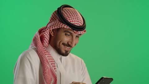 Watching enjoyable movies and series, browsing social media, using modern technology and techniques, a portrait of a Saudi Gulf Arab man wearing traditional attire and a ghutrah using a tablet, green background, chroma.