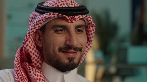 استخدام تطبيق الهاتف المحمول، رجل عربي خليجي سعودي يرتدي الثوب التقليدي والشماغ يمسك الجوال بيده يجلس على الاريكة، تصفح وسائل التواصل الاجتماعي