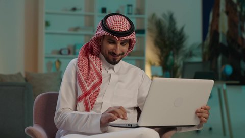 إنجاز المهام المطلوبة عبر اللابتوب، ادارة الأعمال عن بعد، التطوروالتكنولوجيا الحديثة، رجل عربي خليجي سعودي يرتدي الثوب التقليدي والشماغ  يستخدم الحاسوب المحمول، وظائف ومهن سعودية