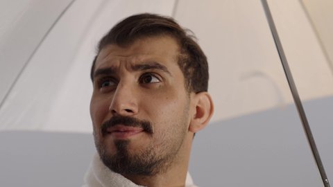 بورتريه مقرب لرجل عربي خليجي سعودي يرتدي ملابس الاحرام يحمل بيده مظلة للحماية من أشعة الشمس و يقوم بشرب الماء، زيارة بيت الله الحرام في مكة المكرمة، الركن الخامس من أركان الاسلام، آداء مناسك الحج والعمرة، خلفية رمادية