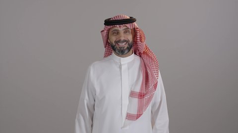 التعبير عن الإعجاب والتقدير، رفع اليد بعلامات الجودة والقبول، الشعور بالرضا والاستحسان، بورتريه لرجل عربي خليجي سعودى مبتسم يرتدى الثوب التقليدى والشماغ يرفع يده للأعلى ينظر إلى الكاميرا بإيماءات السعادة والسرور، مفهوم الرجولة والاناقة، خلفية رمادية
