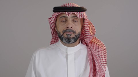 تعابير وإشارات لطلب التوقف و عدم الاقتراب، بورتريه لرجل عربي خليجي سعودى يرتدى الثوب التقليدى والشماغ يرفع يده للأعلى ينظرالى الكاميرا بإيماءات الجدية والحزم، الإمتناع عن فعل شيء ما، خلفية رمادية