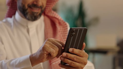 استخدام التطبيقات الحديثة و التسويق الألكتروني, رجل عربي خليجي سعودي يرتدي الثوب التقليدي والشماغ يستخدم الجوال, برامج التواصل الاجتماعي عبر الهاتف المحمول، التواصل مع الأصدقاء