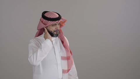 آلام الرقبة والعامود الفقري، بورتريه لرجل عربي خليجي سعودي يرتدي الشماغ والثوب التقليدي ويضع يده على رقبته، إيماءات وجه ويدين تدل على الوجع والألم، التعب والإرهاق والشد العضلي، الحاجة إلى العلاج، خلفية رمادية