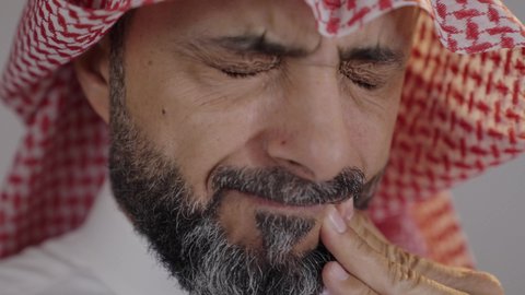 تسوس الأضراس وإلتهاب اللثه، طلب العلاج و المساعده، بورتريه لرجل عربي خليجي سعودى يرتدي الثوب التقليدي والشماغ يضع يديه على خده ويغمض عينيه بإيماءات الشعور بألم الأسنان, خلفية رمادية
