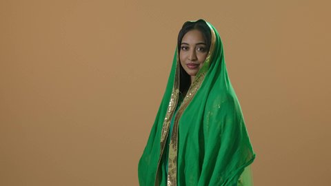 Wearing the Eastern Province attire during national occasions and holidays, on the day we began in 1727 AD, looking at the camera, a portrait of a smiling Arab Gulf Saudi woman wearing the shayla and the green bisht in commemoration of the founding of the first Saudi state on February 22, a full-body image, brown background.