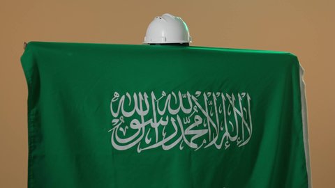 بورتربه من الخلف لمهندسة عربية خليجية سعودية ترتدي سترة الحماية والخوذة البيضاء تضع علم المملكة على كتفيها، إحياء ذكرى اليوم الوطني السعودي في 23 سبتمبر, دورالمهندسيين في التطورالعمراني, الاحتفال بيوم العلم 11 مارس, خلفية بنية