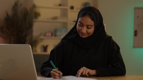 مساهمة المرأة في تطور القطاع الهندسي، مهندسة عربية خليجية سعودية محجبة ترتدي العباءة السوداء تقوم بالعمل على التابلت و تدوين الملاحظات بإيماءات الاندماج والتركيز، إنجاز المهام اليومية في المكتب بجانب خوذتها, مهن ووظائف نسائية سعودية