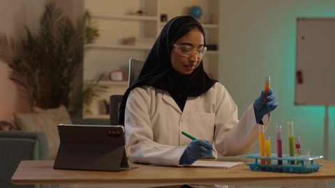 مفهوم العلوم الطبية المخبرية المتطورة, طبيبة صيدلانية عربية خليجية سعودية محجبة ترتدي المعطف الطبي الأبيض تمسك أمبولات التحاليل في المختبرات الطبية الحديثة، تدوين نتائج الفحوصات الطبية، مهن ووظائف نسائية