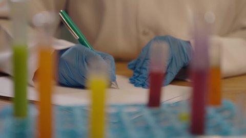 استخدام الانابيب الزجاجية لتحليل العينات المختلفة، طبيبة مخبرية خليجية ترتدي القفازات الطبية تقوم بتدوين نتائج الفحوصات الطبية، اخصائية الطب المخبري، تحاليل تشخيصية كيميائية