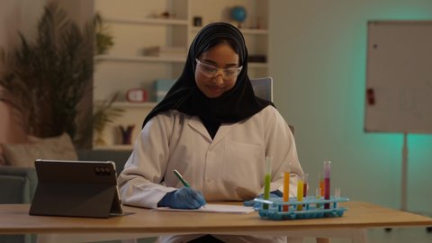 الادوية والمستلزمات الطبية، مفهوم الصيدلة والرعاية الصحية، التشييك على قائمة الأدوية, طبيبة صيدلانية عربية خليجية سعودية محجبة ترتدي المعطف الطبي الأبيض تقوم بكتابة الوصفات العلاجية بجانب التابلت، مهن ووظائف نسائية