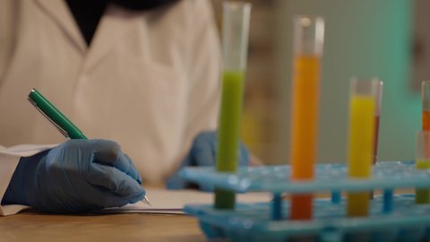 طبيبة مخبرية خليجية ترتدي القفازات الطبية تقوم بتدوين نتائج الفحوصات الطبية، استخدام الانابيب الزجاجية لتحليل العينات المختلفة ،اخصائية الطب المخبري، تحاليل تشخيصية كيميائية