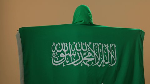 يوم بدينا 22 فبراير, الاحتفال بذكرى اليوم الوطني السعودي 23 سبتمبر، يوم العلم 11 مارس، ارتداء الزي الشعبي للمنطقة الوسطى في مناسبة وطنية, بورتريه من الخلف لامرأة عربية خليجية سعودية ترتدي الشيلة والبشت الأخضر تضع على كتفيها علم المملكة، خلفية بنية
