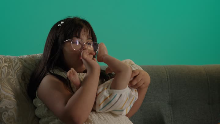 بورتريه لطفلة سعودية مصابة بمتلازمه داون ترتدى النظارة تلعب بالدمية، قضاء وقت ممتع بالالعاب، اللعب واللهو والمرح بحماس ونشاط، خلفية حضراء