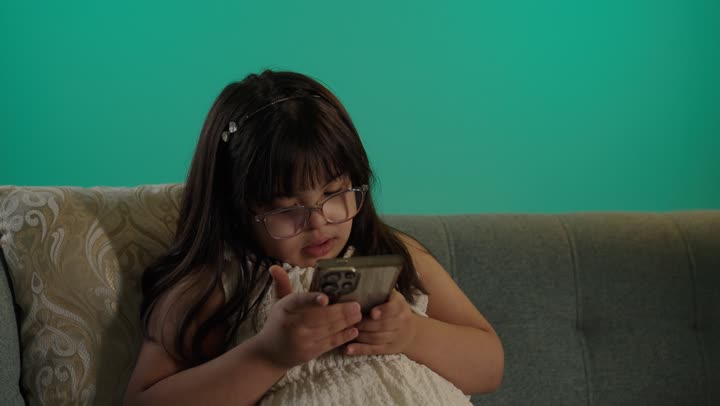 تلقي اهتمام كبير من خلال التعليم عن بعد، بورتريه لطفلة سعودية مصابة بمتلازمه داون ترتدى النظارة تمسك الهاتف، التعلم عن طريق الانترنت، خلفية حضراء