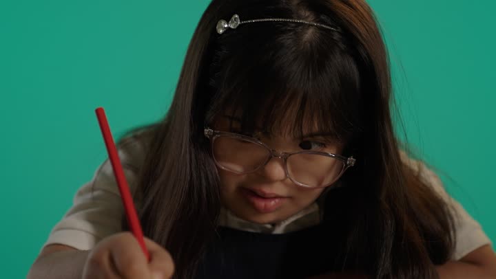 Development of mental and intellectual abilities for people with determination, a portrait of a Saudi girl with Down syndrome coloring, nurturing and developing children's skills, having a good time, green background.