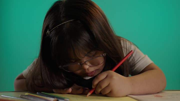 إيماءات التركيز والاستمتاع بالرسم والتلوين، بورتريه لطفلة سعودية مصابة بمتلازمه داون تمسك الألوان، رعاية و تطوير مهارات الأطفال، قضاء وقت ممتع فى المنزل، خلفية خضراء