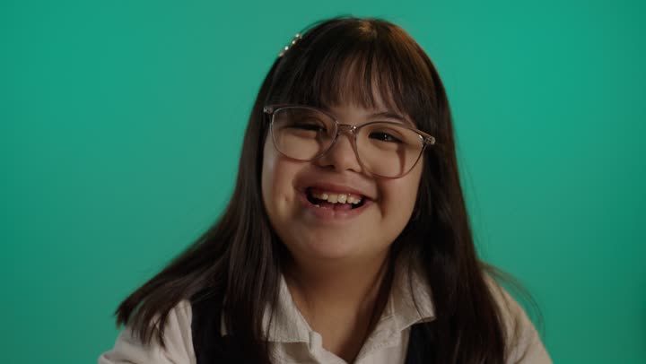 وقت التسلية والترفيه، بورتريه لطفلة عربية خليجية سعودية مصابة بمتلازمه داون مبتسمة ترتدى نظارة تلعب باقلام التلوين، رعاية و تطوير مهارات الأطفال، خلفية خضراء