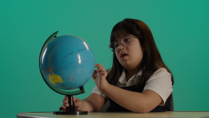 The concept of research and exploration around the world, a Saudi girl with Down syndrome wearing glasses holding a globe model in her hand, going on a tourist trip.