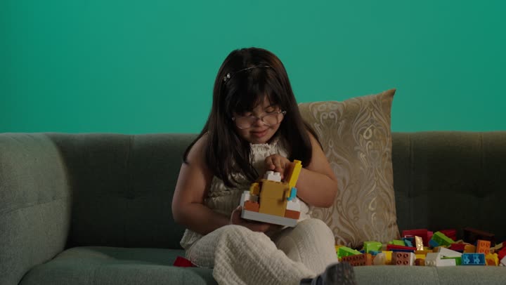 A Saudi girl with Down syndrome is playing with blocks, the concept of caring for hobbies, spending enjoyable time at home, developing mental and intellectual skills, expressions of happiness and joy.