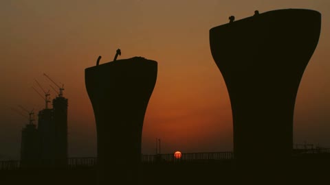 غروب الشمس أمام أبراج دعم الجسر قيد الإنشاء في مشروع جسر المنامة الشمالي، الهندسة الفنية المعمارية للأبراج وناطحات السحاب في البحرين, التطور والتقدم العمراني البحريني, معالم وأماكن السياحة المشهورة،  شركة خليج البحرين