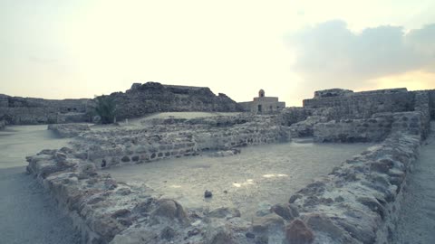 آثار قلعة البحرين تحت سماء غائمة، تل أثري يتكون من طبقات استيطان بشري متعاقبة،  مبانٍ سكنية وتجارية وعسكرية ودينية، عاصمة لحضارة دلمون، مدرج في قائمة اليونسكو للتراث العالمي ويضم متحفًا، ميناءً تجاريًا رئيسيًا بين حضارات بلاد ما بين النهرين والهند