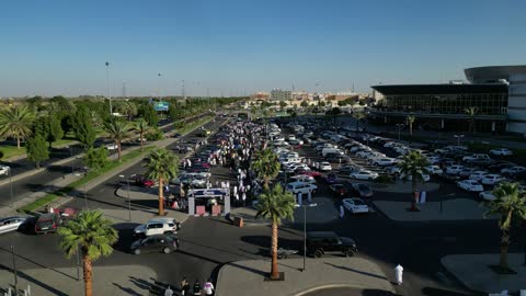 The movement of internal trade in the Kingdom of Saudi Arabia, attracting customers and consumers through a distinctive car display method, a market for buying and selling used cars, drone photography of rows of vehicles from various global brands in a car exhibition area in the Tabuk region.