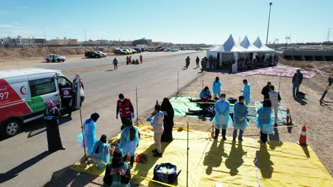 أفراد يرتدون زي المسعفين والأطباء، تدريباً أو مناورة طوارئ طبية في الهواء الطلق، تنظمها هيئة الهلال الأحمرفيالمملكة العربية  السعودية أو جهة حكومية أخرى في المملكة العربية السعودية،  التعاون بين جهات متعددة، المعدات سيارة إسعافر، مخاريط مرورية لتنظيم الموقع