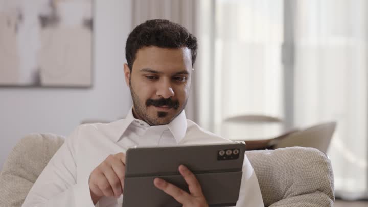 استخدام التكنولوجيا والتقنية الحديثة، متابعة الأفلام والمسلسلات الممتعة، تصفح مواقع التواصل الاجتماعي, رجل عربي خليجي سعودي يرتدي الثوب التقليدي يجلس على الاريكة يستخدم التابلت