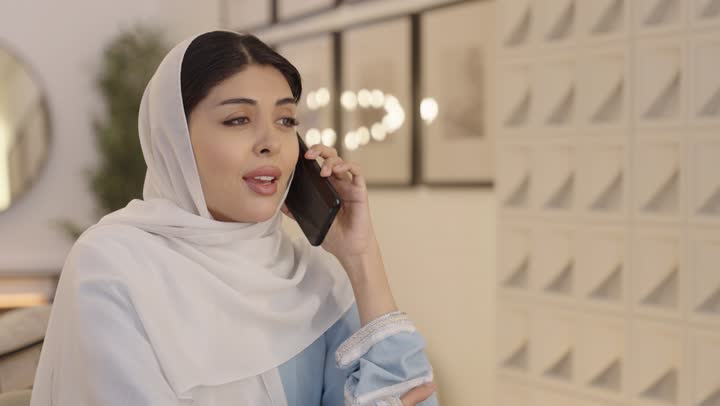 The use of modern technology, a Gulf Arab Saudi woman wearing a hijab is talking on her mobile phone, chatting with family and friends, spending enjoyable time.