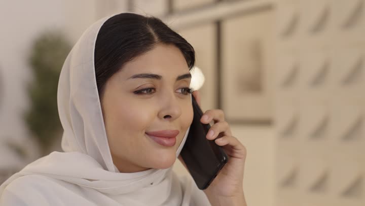 امراة عربية خليجية سعودية محجبة تقوم بالتحدث عبر الهاتف المحمول، إجراء مكالمة هاتفية عبر الجوال, التواصل مع الاصدقاء، استخدام جهاز تقنى حديث