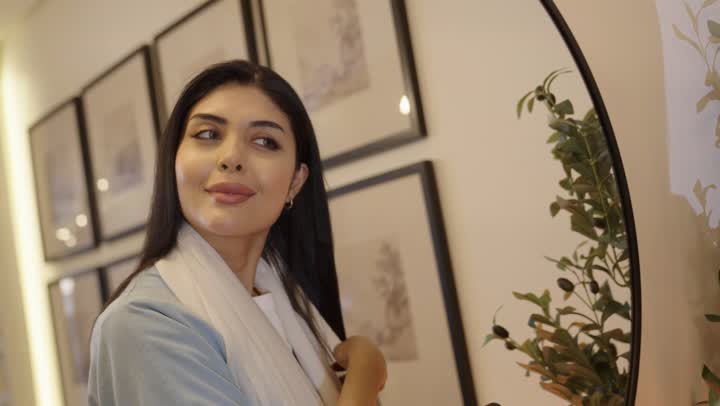 مفهوم العناية والاهتمام بالجمال والأناقة والمظهر الخارجي، تمشيط وترتيب الشعر، مفهوم الانوثه والنعومه، أمرأة عربيه خليجيه سعودية ترتدي عباءة بالون الازرق الفاتح تقوم بتصفيف شعرها امام المرأة باستخدام فرشاة الشعر