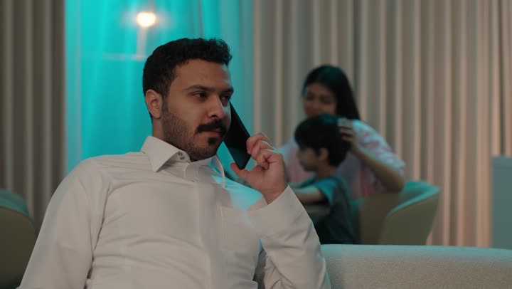 إجراء اتصال هاتفي عبر الجوال, التواصل مع الأصدقاء والأهل, مشاركة الأخباروالأحاديث الجيدة, شاب عربي خليجي سعودي يرتدي الزي التقليدي يجلس على الاريكة يمسك الهاتف المحمول بيده