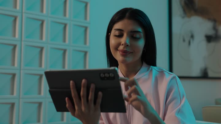 Completing tasks remotely, online shopping, tablet applications, using modern and advanced devices and technologies, an Arab Gulf Saudi woman wearing casual attire is tapping on a mobile tablet.