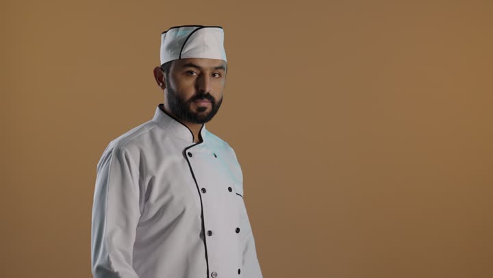 احتراف مهنة الطهي، الوقوف بتعابير أيدي متقاطعة ,طهي الطعام السعودي، بورتريه لشيف عربي خليجي سعودي يرتدي يونيفورم الطبخ ينظر إلى الكاميرا بثقة وفخر, خلفية بنية