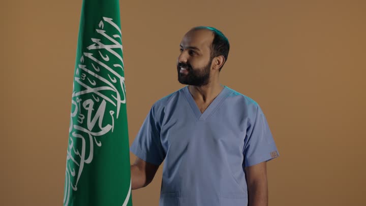 The concept of loyalty, love for the homeland, and pride in belonging to Saudi Arabia, a side portrait of a Saudi Gulf Arab nurse wearing a uniform and gloves holding the Kingdom's flag, celebrating the anniversary of Saudi National Day on September 23 and the national holiday, with a brown background.