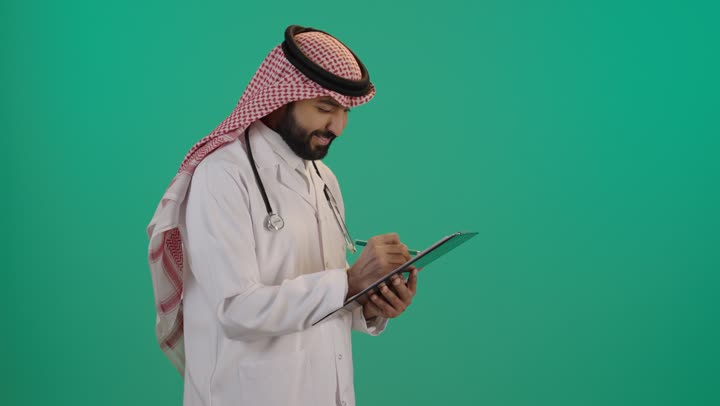 The concept of healthcare in Saudi Arabia, a portrait of an Arab Gulf Saudi doctor wearing traditional attire and a white coat, using a stethoscope and writing on a file, providing therapeutic services in medical centers and hospitals, recording and documenting patient information and files, green background.