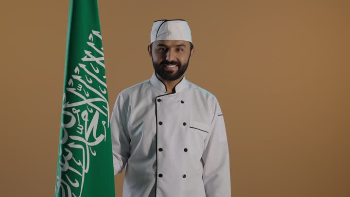 تحقيق النمو والتطور بسواعد أبناء الوطن, الإحتفال بذكرى اليوم الوطني السعودي 23 سبتمبر والعيد الوطني، بورتريه لشيف عربي خليجي سعودي يرتدي الزي الرسمي الخاص بمزاولة مهنة الطباخ بمسك علم المملكة، الاخلاص والولاء للبلاد، خلفية بنية