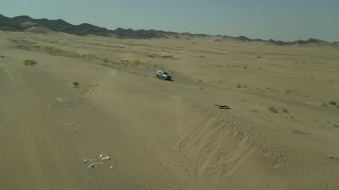 Safari adventure on the sand dunes in the Kingdom of Saudi Arabia, drone footage of an Isuzu off-road vehicle on the golden desert sands, the sand hills and rock formations in the Arab deserts, recreational activities for driving in desert areas.